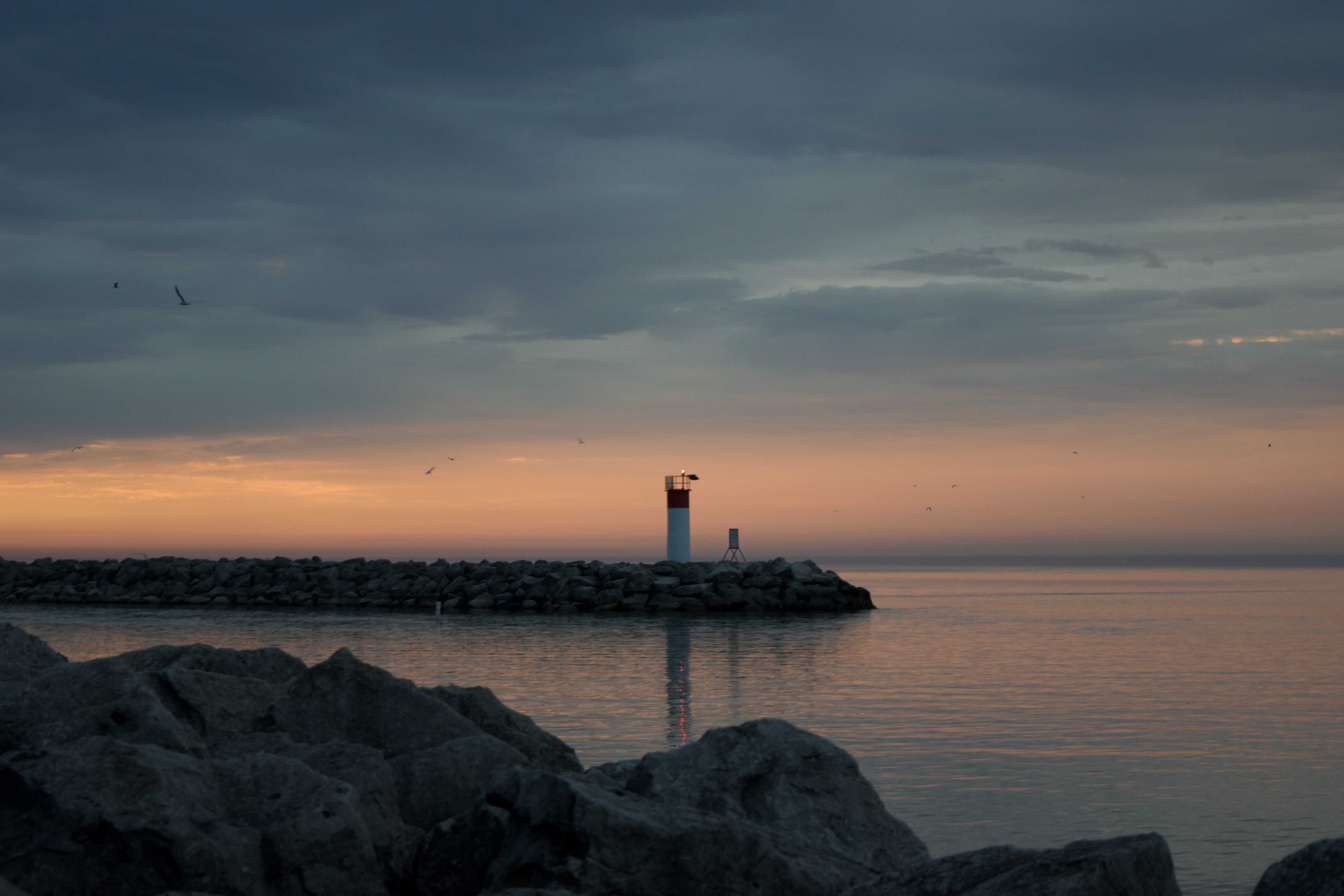 A lighthouse on a peer in the distance during the sunset