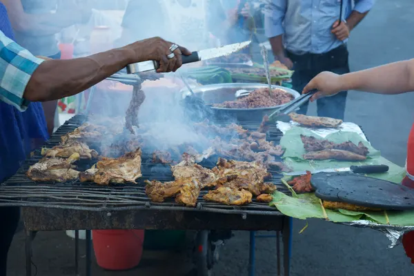 Street vendors with a knife over a grill covered in chicken