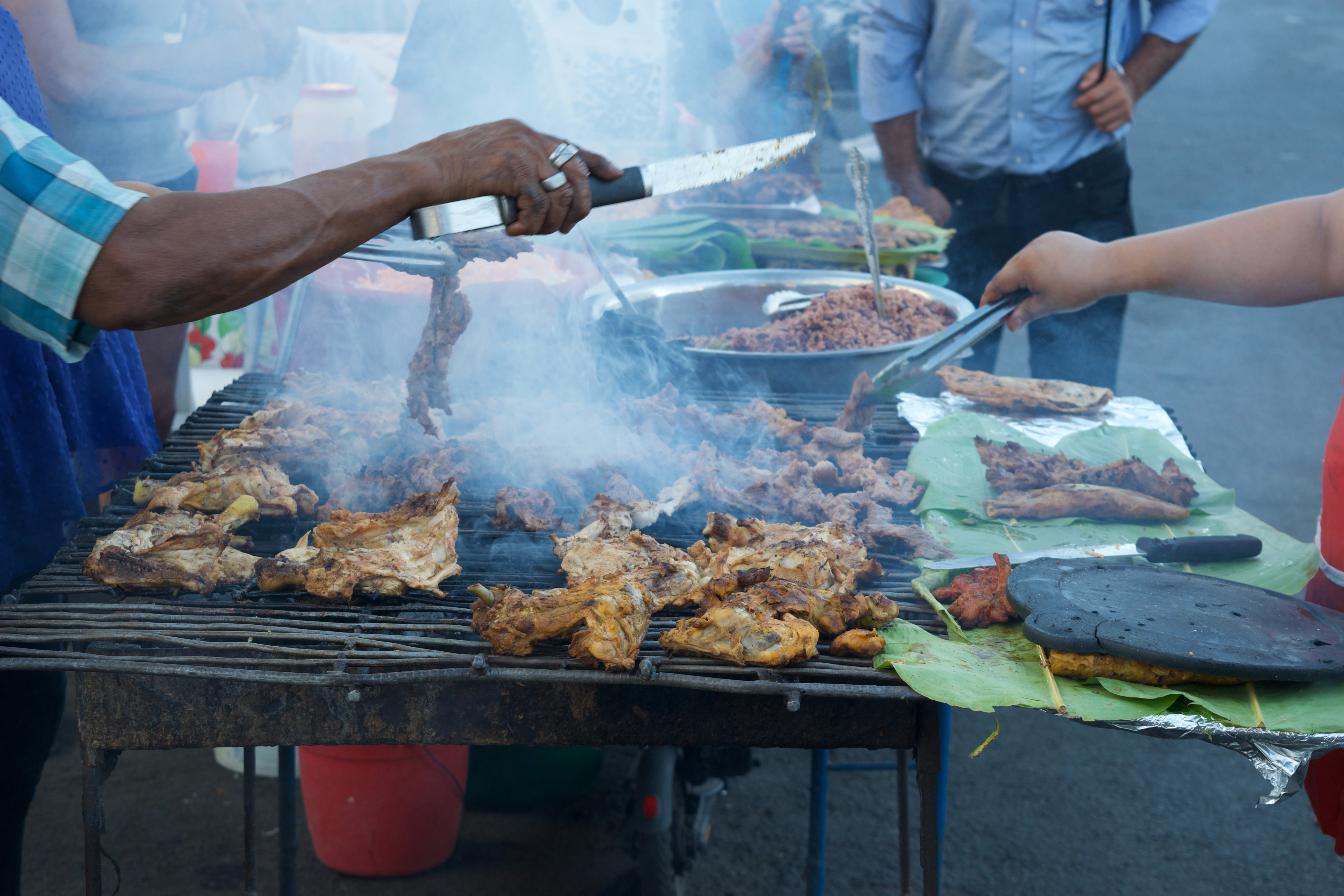 Street vendors with a knife over a grill covered in chicken